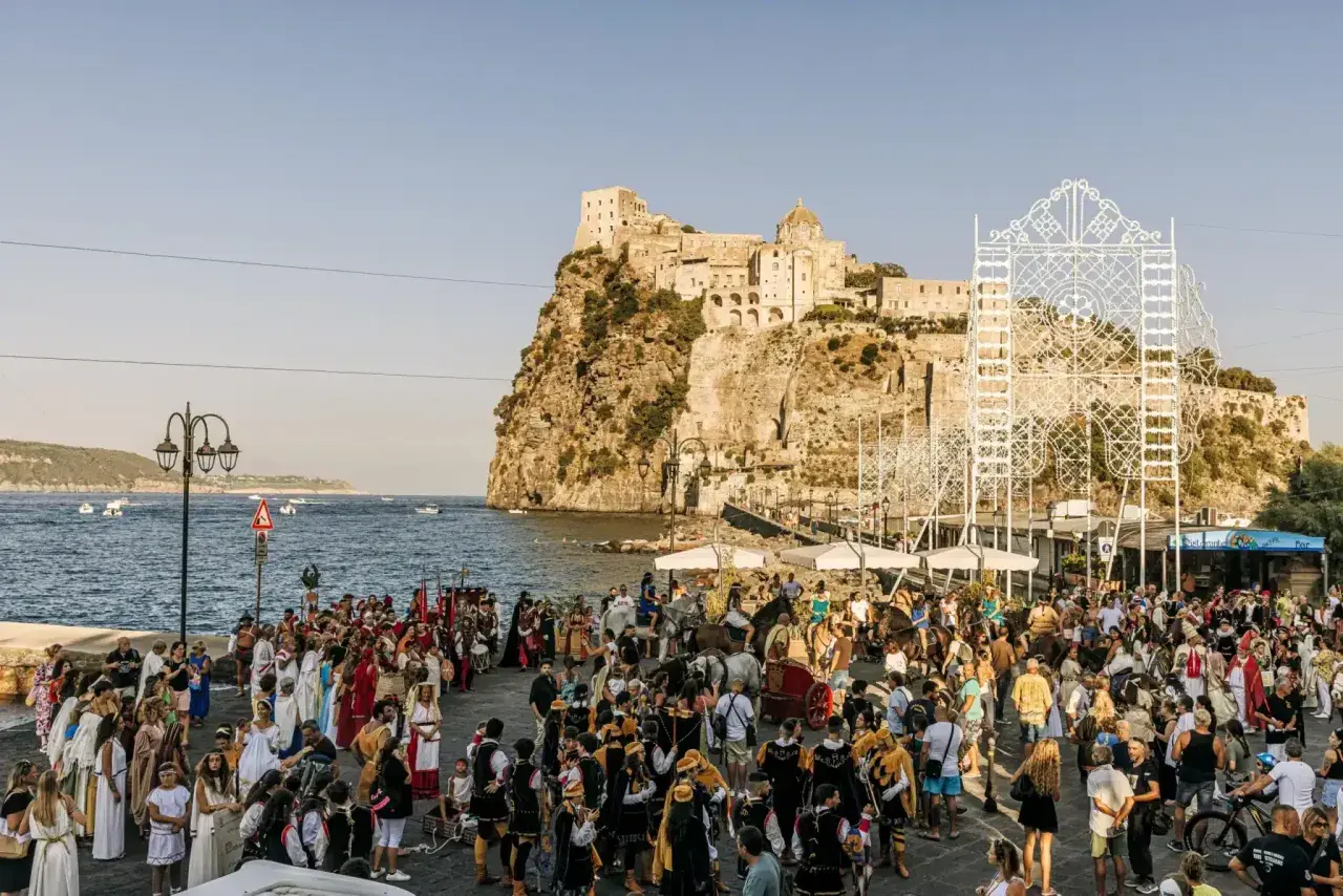 Festa in costume sul lungomare, con il castello sullo sfondo. La spiaggia degli inglesi è animata da figuranti e spettatori.