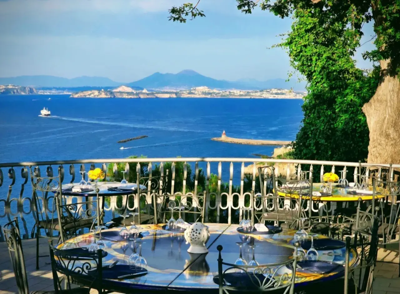 Tavoli apparecchiati con vista mare, un invito a cenare in uno dei ristoranti di Casamicciola. Il Vesuvio sullo sfondo.