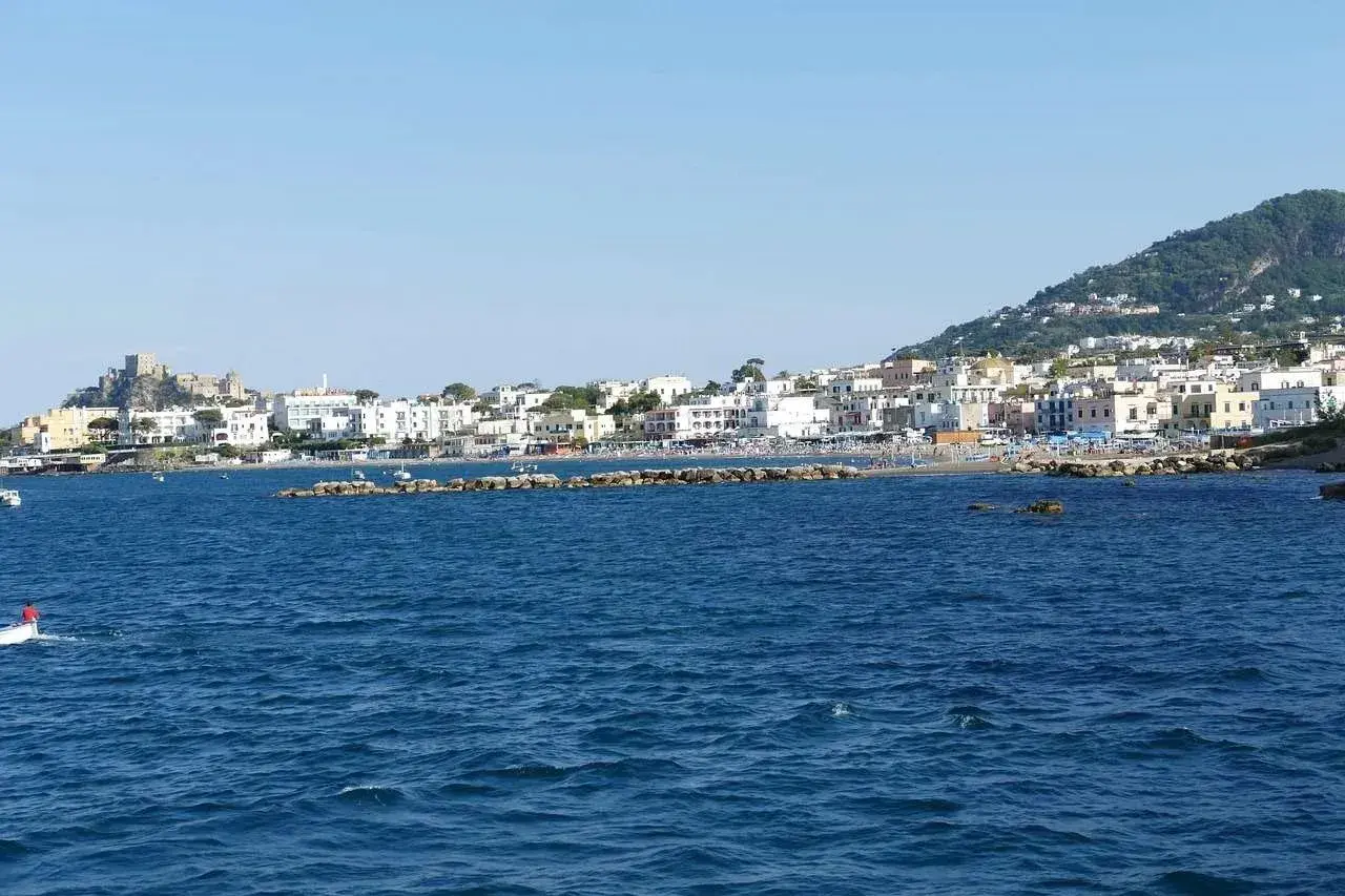 La costa di Ischia vista dal mare, con il castello Aragonese in lontananza. Immagina i traghetti Formia Ischia che ti portano qui.