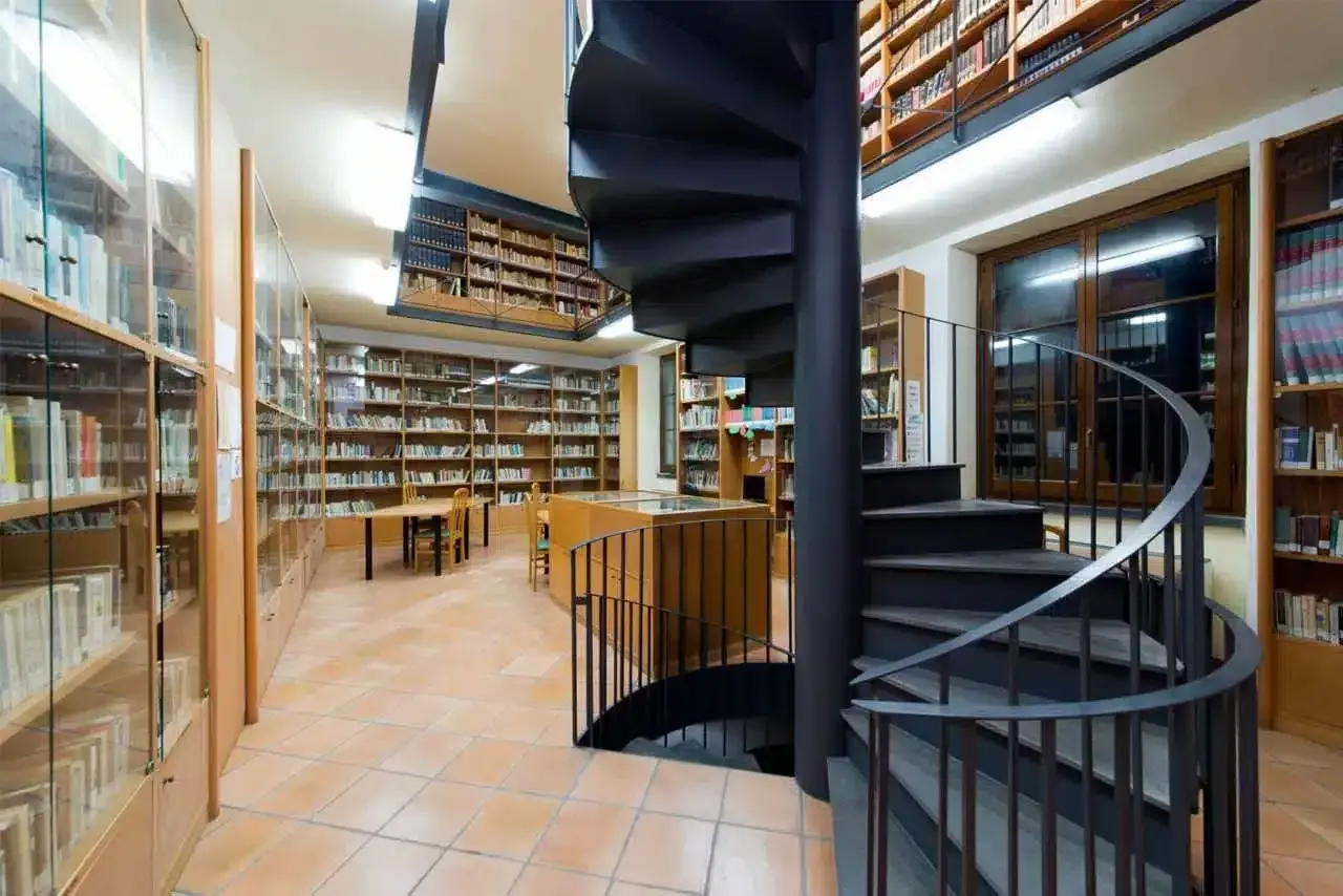 Interno della biblioteca antoniana ischia con scaffali pieni di libri, tavoli e una scala a chiocciola nera.