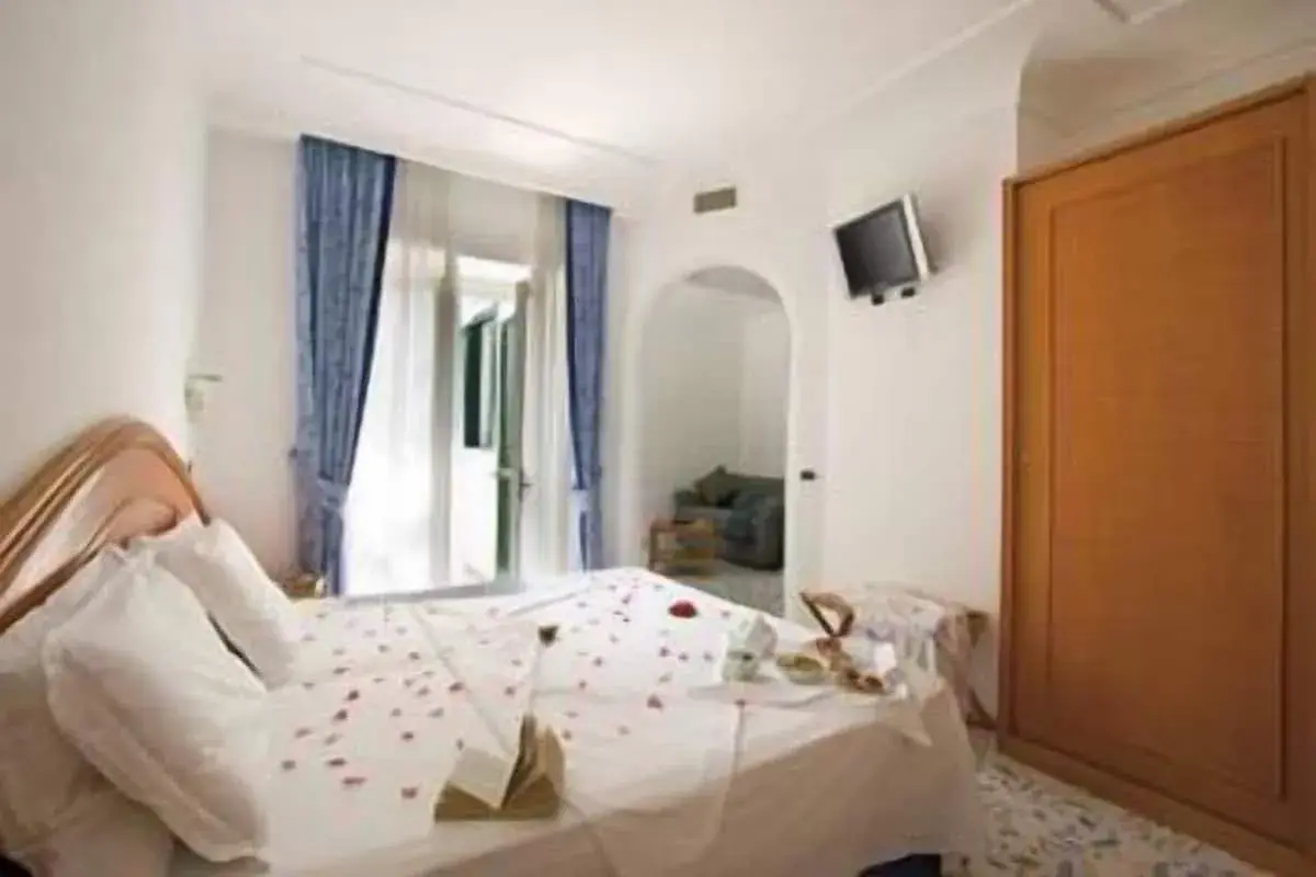 Camera accogliente con letto decorato con petali di rosa, un tavolino con colazione e un armadio in legno. Un'oasi di relax al hotel terme mediterraneo Ischia.