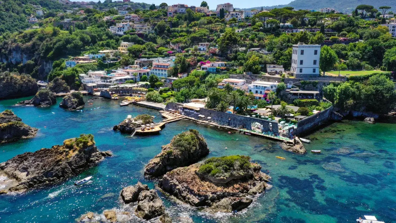 Baia di Cartaromana con rocce e acque cristalline. Case arroccate sulla collina. Scopri come arrivare a questa incantevole spiaggia.
