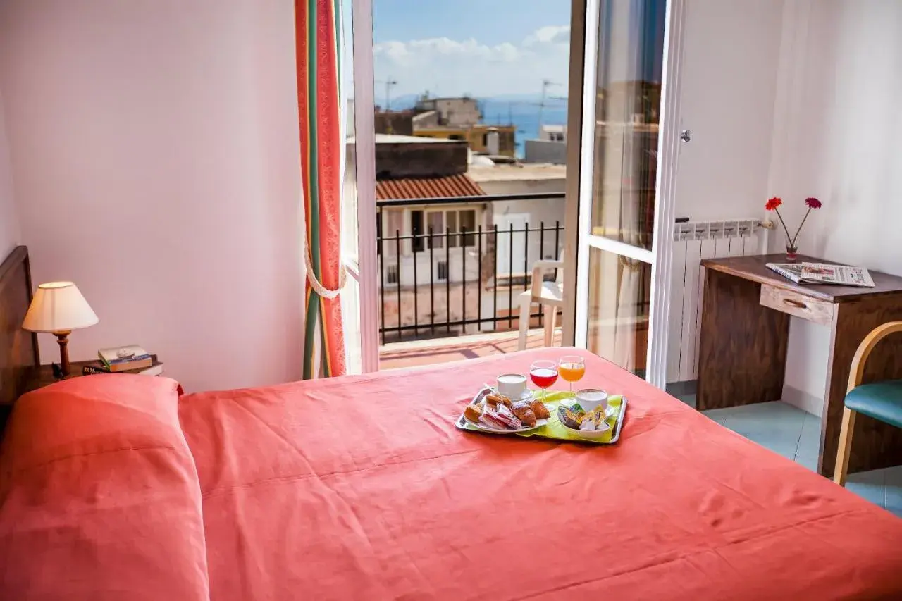 Camera con letto rosso e vassoio colazione sul letto. Vista mare dal balcone dell'hotel Conte Ischia.