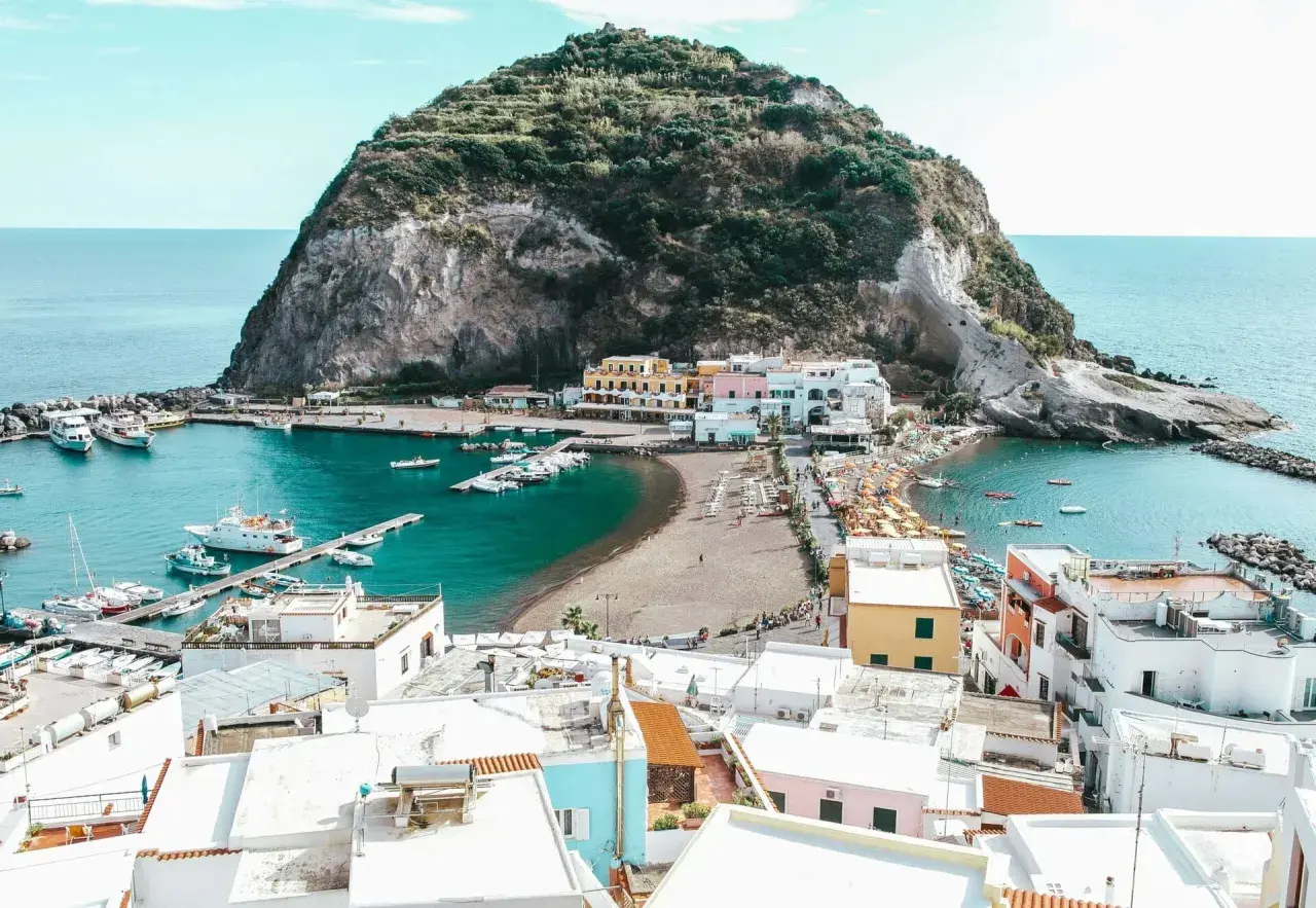 Baia con barche e case colorate a Ischia, con la rocca verde che domina il mare. Le cantine di Ischia offrono un panorama mozzafiato.