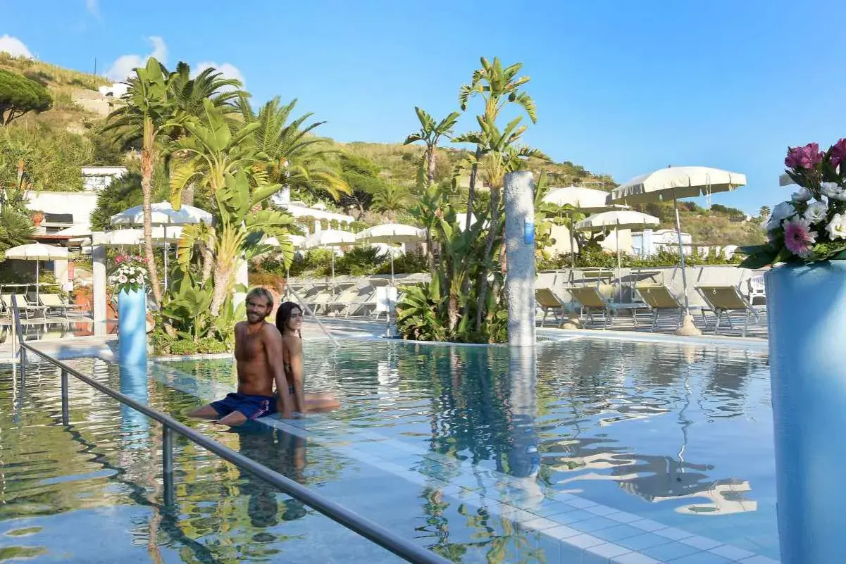 Coppia rilassata in piscina, circondata da palme e lettini, in un resort alle terme Ischia.