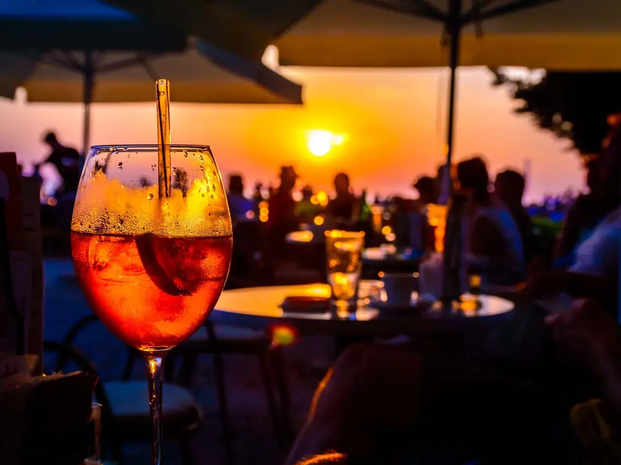 Un aperitivo rinfrescante con vista sul tramonto a Ischia centro sera. Persone sedute ai tavoli, ombrelloni e il sole che cala all'orizzonte.