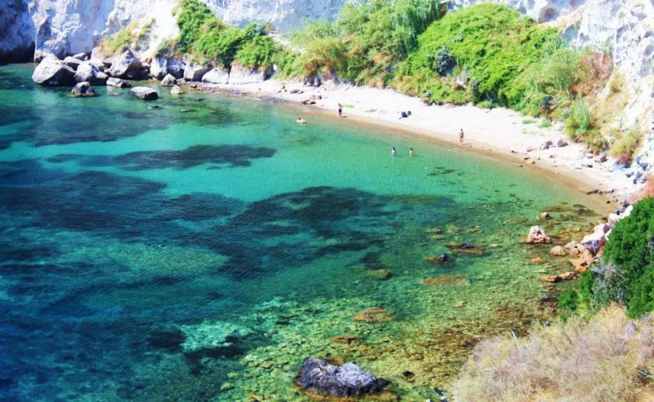 Acque cristalline e sabbia dorata nella spiaggia delle monache, incastonata tra scogliere rocciose e vegetazione rigogliosa.