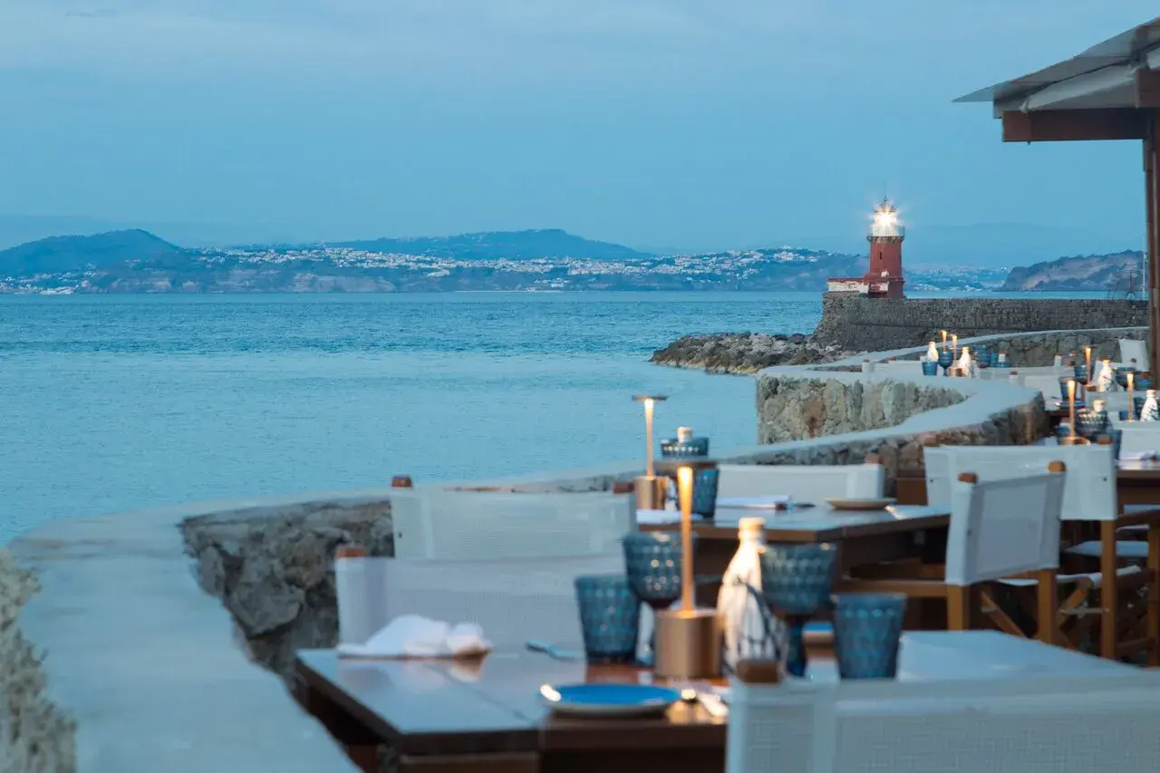 Tavoli apparecchiati con vista sul mare e un faro rosso, un invito a cena a Ischia.