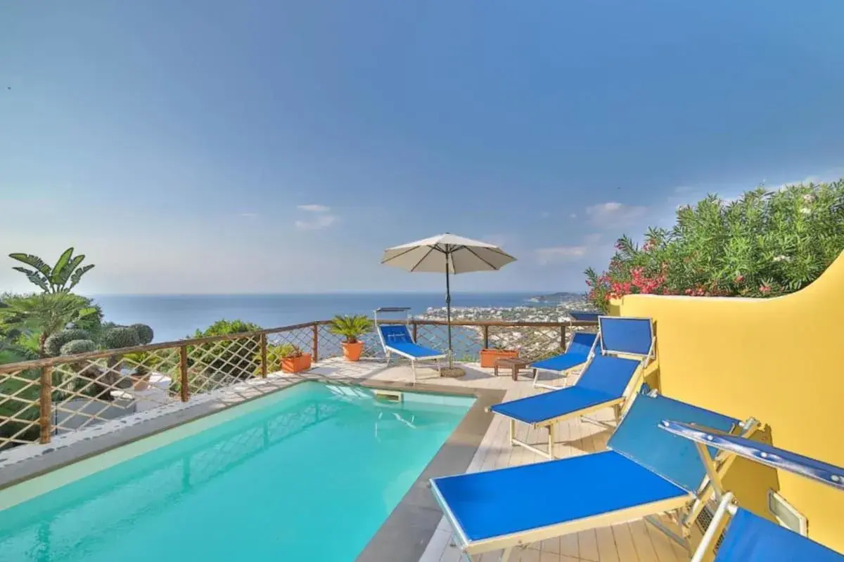 Piscina con lettini blu e vista mare a Ischia. Un angolo di paradiso, un dolce Poseidon che invita al relax.
