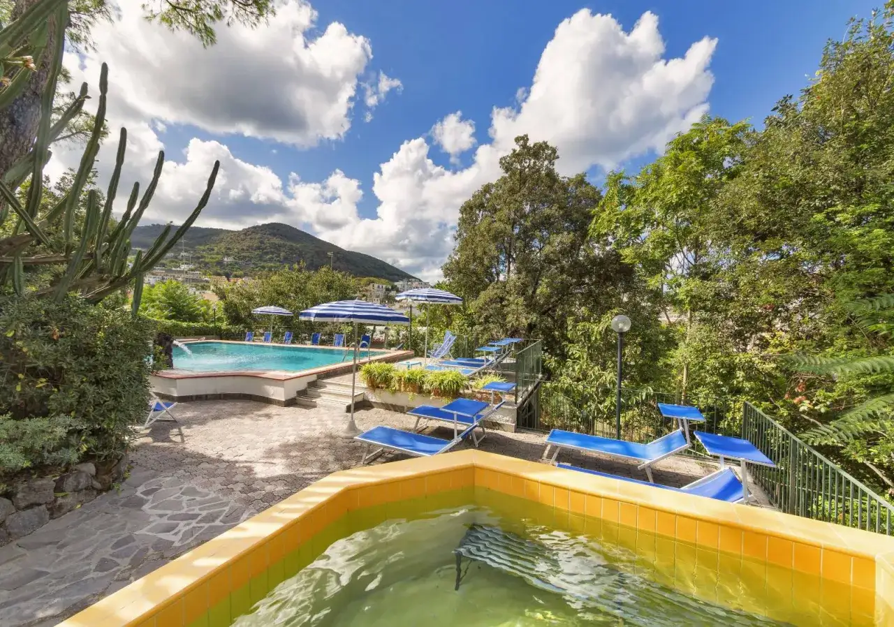 Piscine e lettini blu sotto ombrelloni a righe, con vista collinare. Un angolo di paradiso alla Villa Diana Ischia.