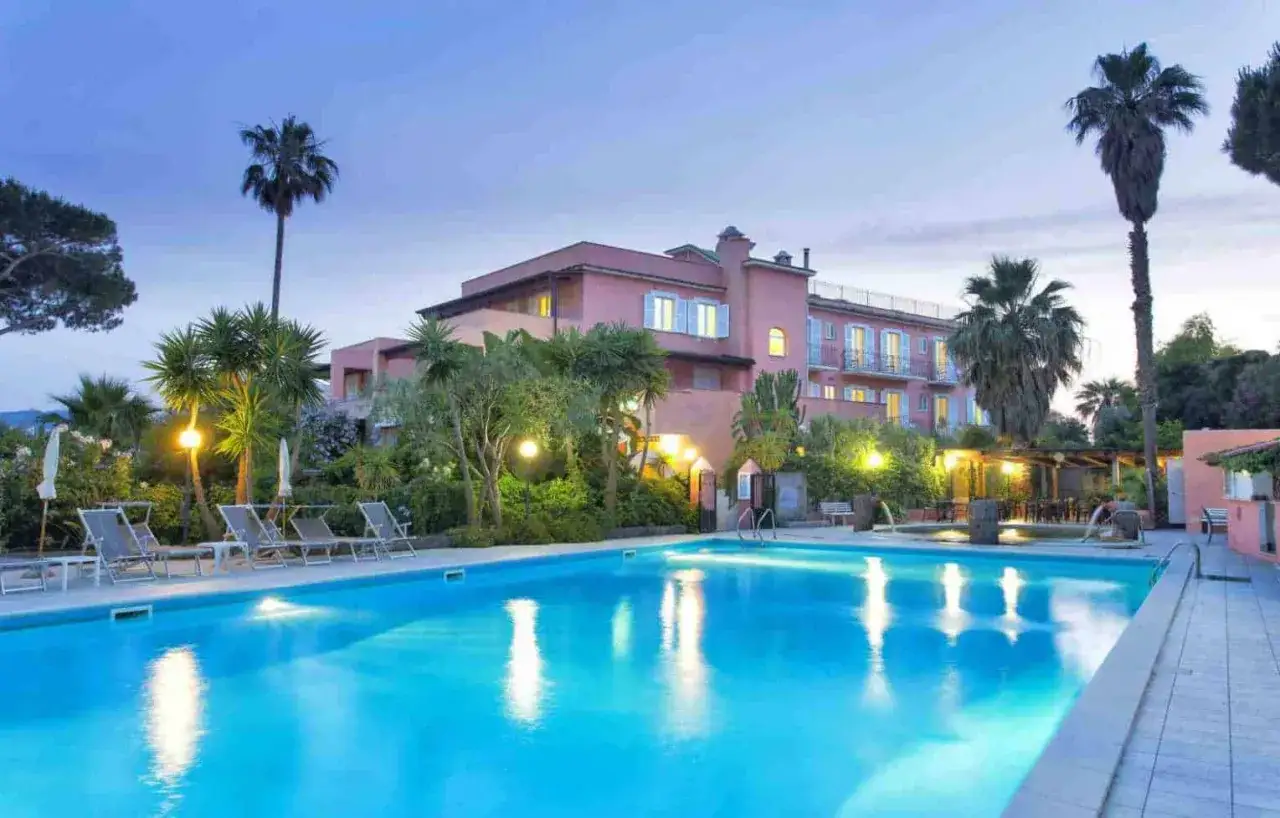 Piscina illuminata e palme al tramonto all'Eden Park Ischia, un'oasi di relax.