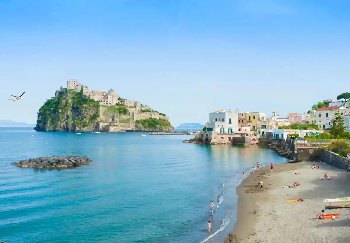 Lidi a Ischia Porto con il Castello Aragonese sullo sfondo. Gente in spiaggia e mare azzurro.