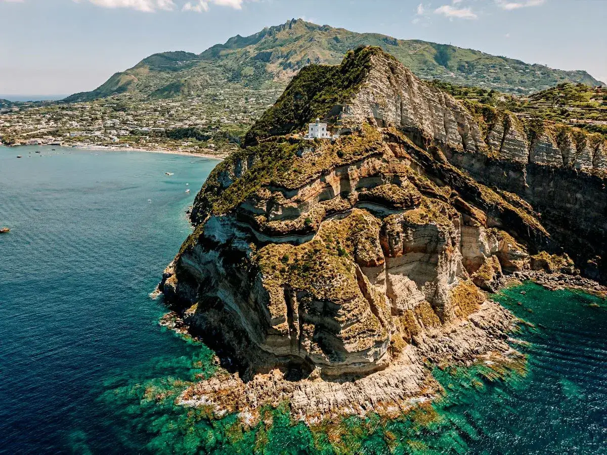 Il faro di Punta Imperatore domina la scogliera rocciosa, con il mare cristallino e la costa verdeggiante sullo sfondo.