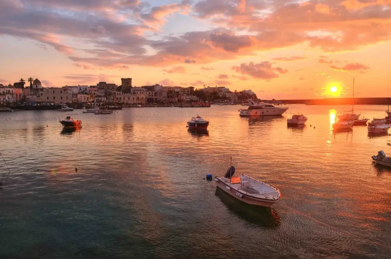 Tramonto infuocato sul lungomare di Forio, Ischia. Barche ormeggiate riflettono i colori caldi del cielo.