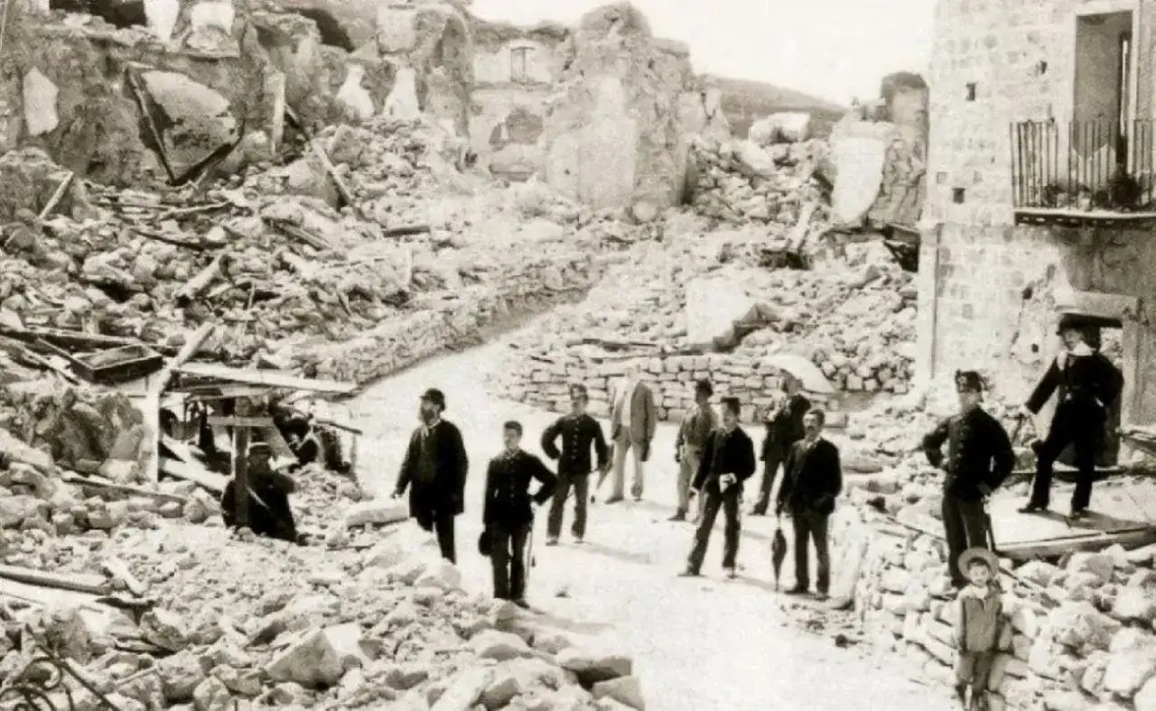 Scene post-terremoto a Ischia. Uomini in abiti d'epoca osservano le macerie di edifici distrutti.