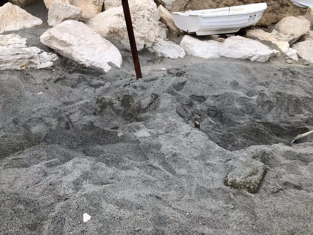 Sabbia scura e rocce bianche sulla spiaggia delle fumarole, con una piccola barca bianca appoggiata.