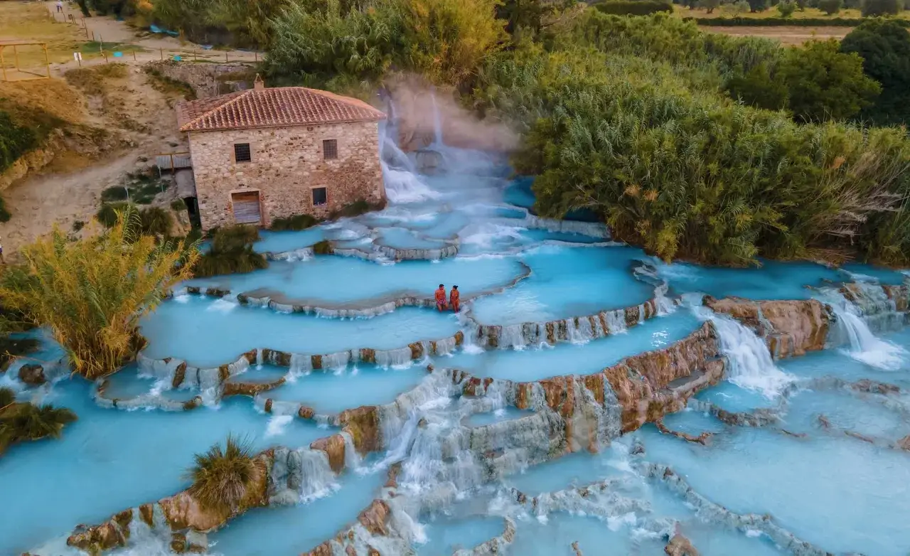 Coppia in un paesaggio naturale di cascate azzurre e rocce, dove l'acqua calda sgorga dalla terra: ecco cosa sono le sorgenti termali.