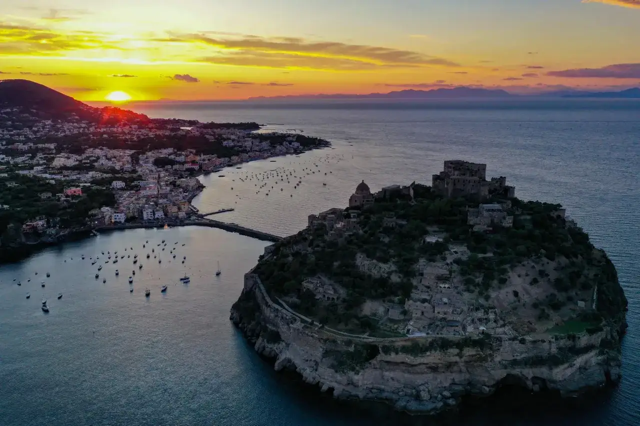 Tramonto dorato su Ischia, con il Castello Aragonese che sembra un nascondiglio dell'amore, circondato dal mare e da un borgo pittoresco.