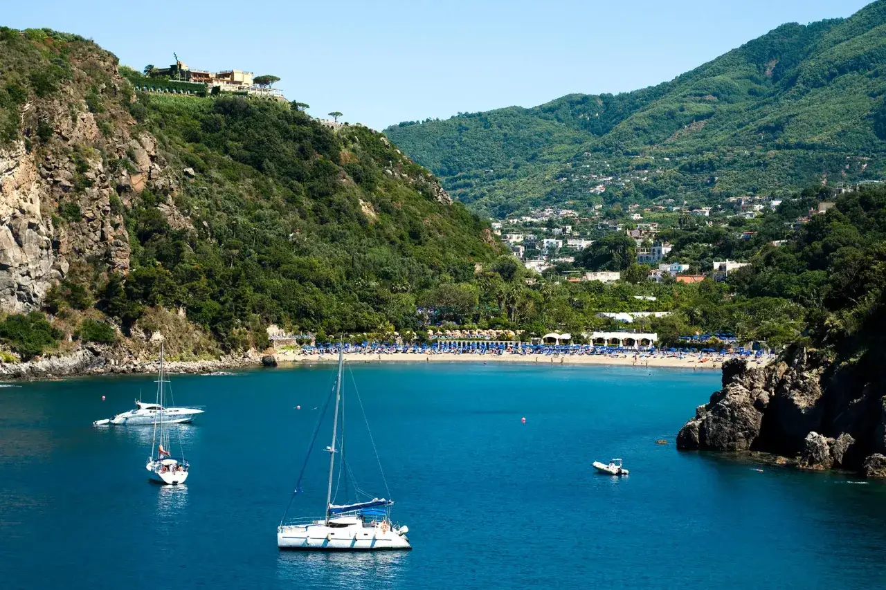 La baia di San Montano con la sua spiaggia attrezzata e le barche a vela. Informazioni sui prezzi per godersi questo paradiso.