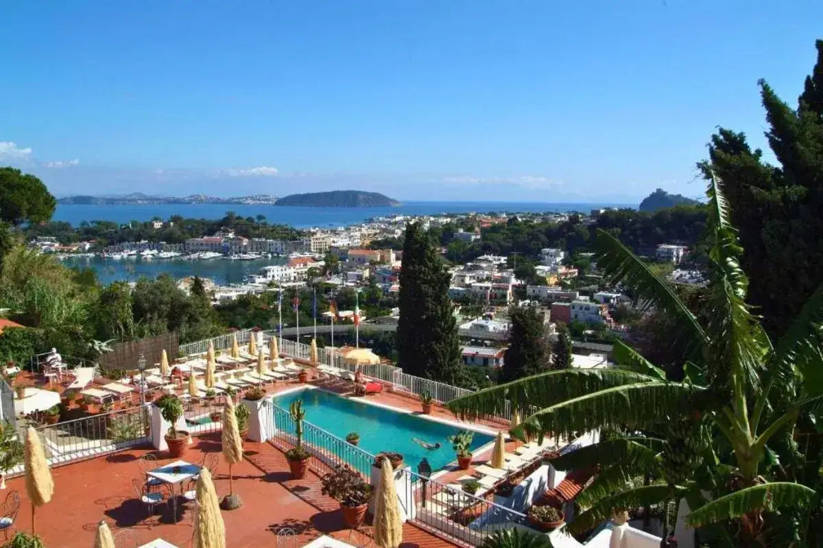 Vista panoramica da un paradiso relais villa janto con piscina, lettini, tavoli e un mare azzurro con barche.