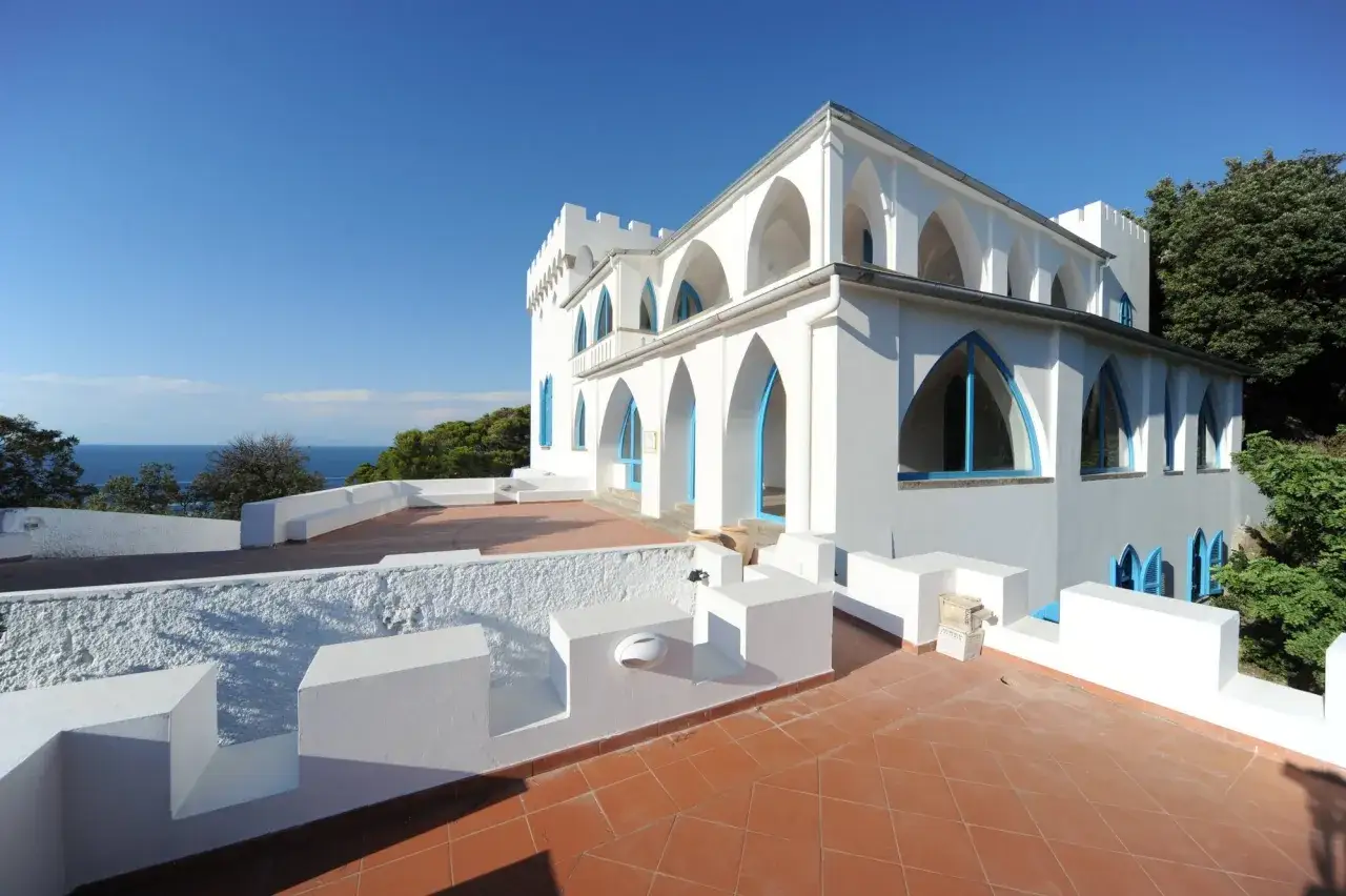 Villa La Colombaia a Ischia, con le sue arcate bianche e le finestre blu, domina il mare sotto un cielo limpido.