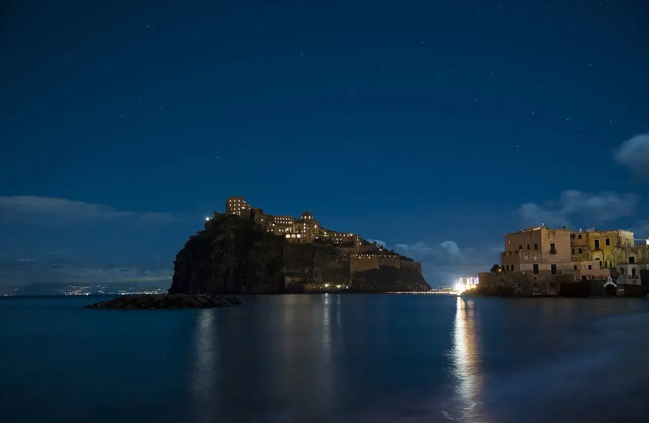 Castello Aragonese illuminato di notte, un'opera di Gabriele Mattera, con il mare calmo e un cielo stellato.