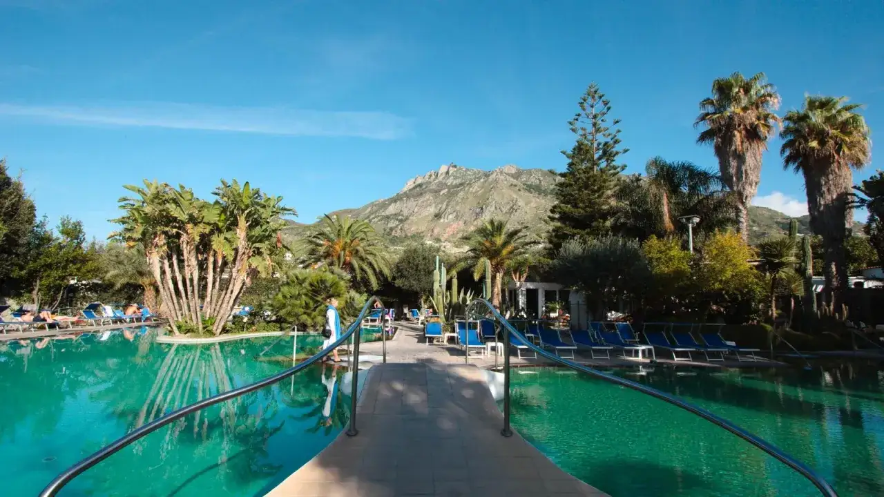 Piscina cristallina e palme rigogliose al Hotel Terme Mediterraneo Ischia, con vista sulle montagne. Relax assicurato.