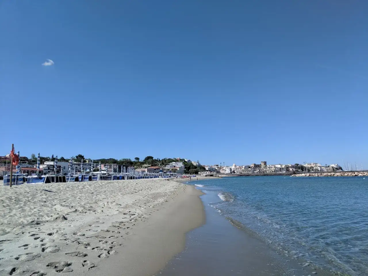 Spiaggia della Chiaia con lettini e ombrelloni pronti per l'estate. Il mare azzurro lambisce la sabbia dorata, mentre sullo sfondo si staglia un pittoresco borgo costiero.