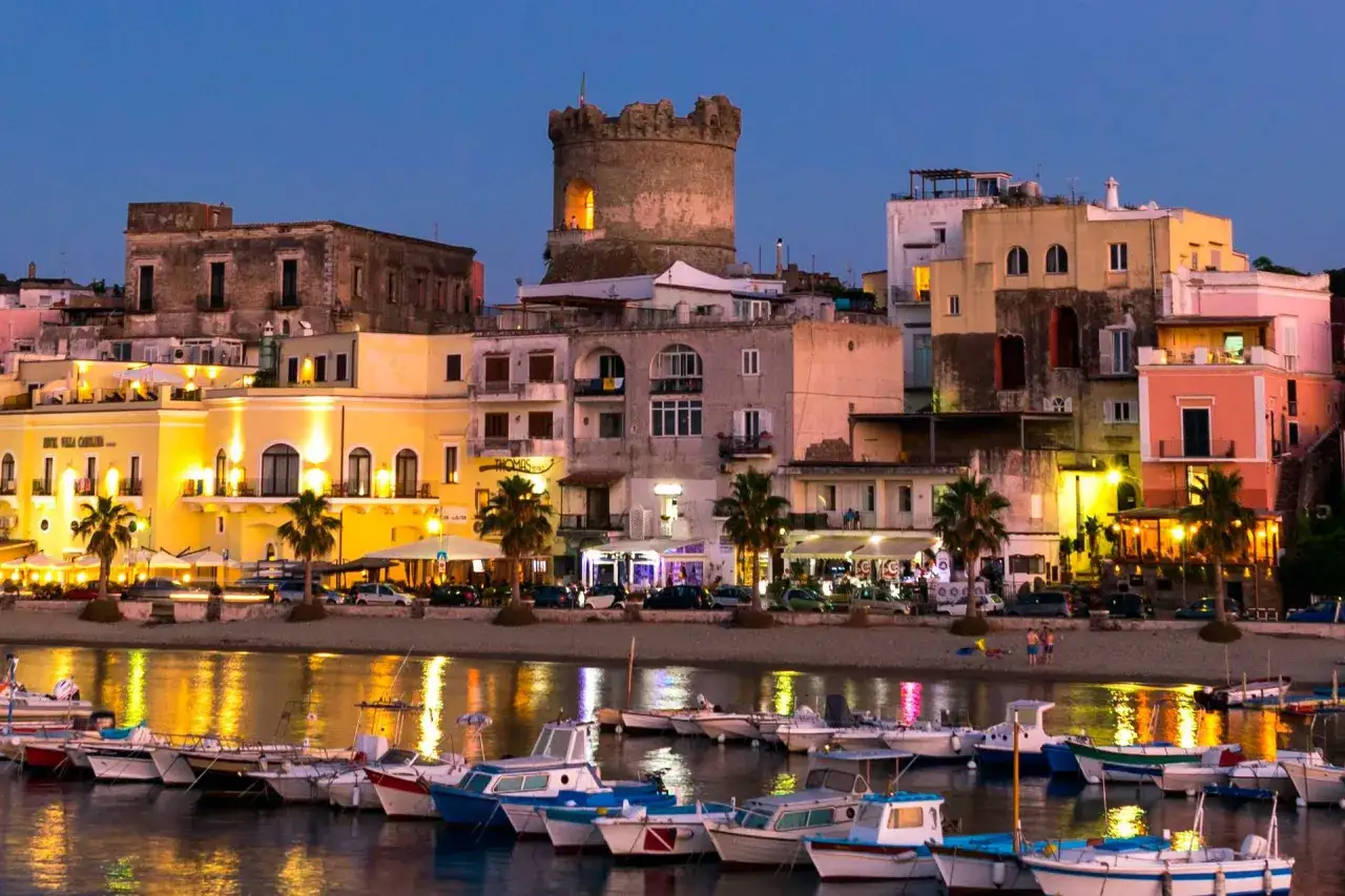 Forio Ischia centro: un borgo marinaro illuminato al tramonto, con barche ormeggiate e un'antica torre che domina il paesaggio.