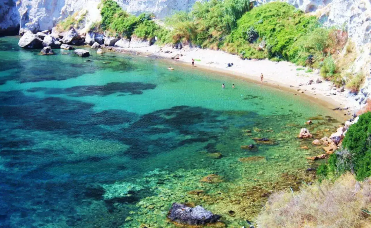 Acque cristalline e sabbia dorata nella spiaggia delle monache, incastonata tra scogliere rocciose e vegetazione rigogliosa.