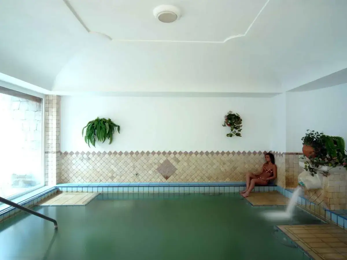 Donna rilassata nella piscina termale dell'Hotel Don Pepe, con cascata e piante verdi.