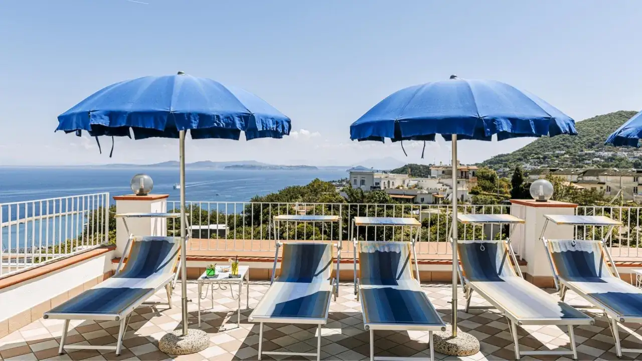Terrazza con lettini e ombrelloni blu, vista mare a Casamicciola. L'hotel Villa d'Orta offre un panorama mozzafiato.