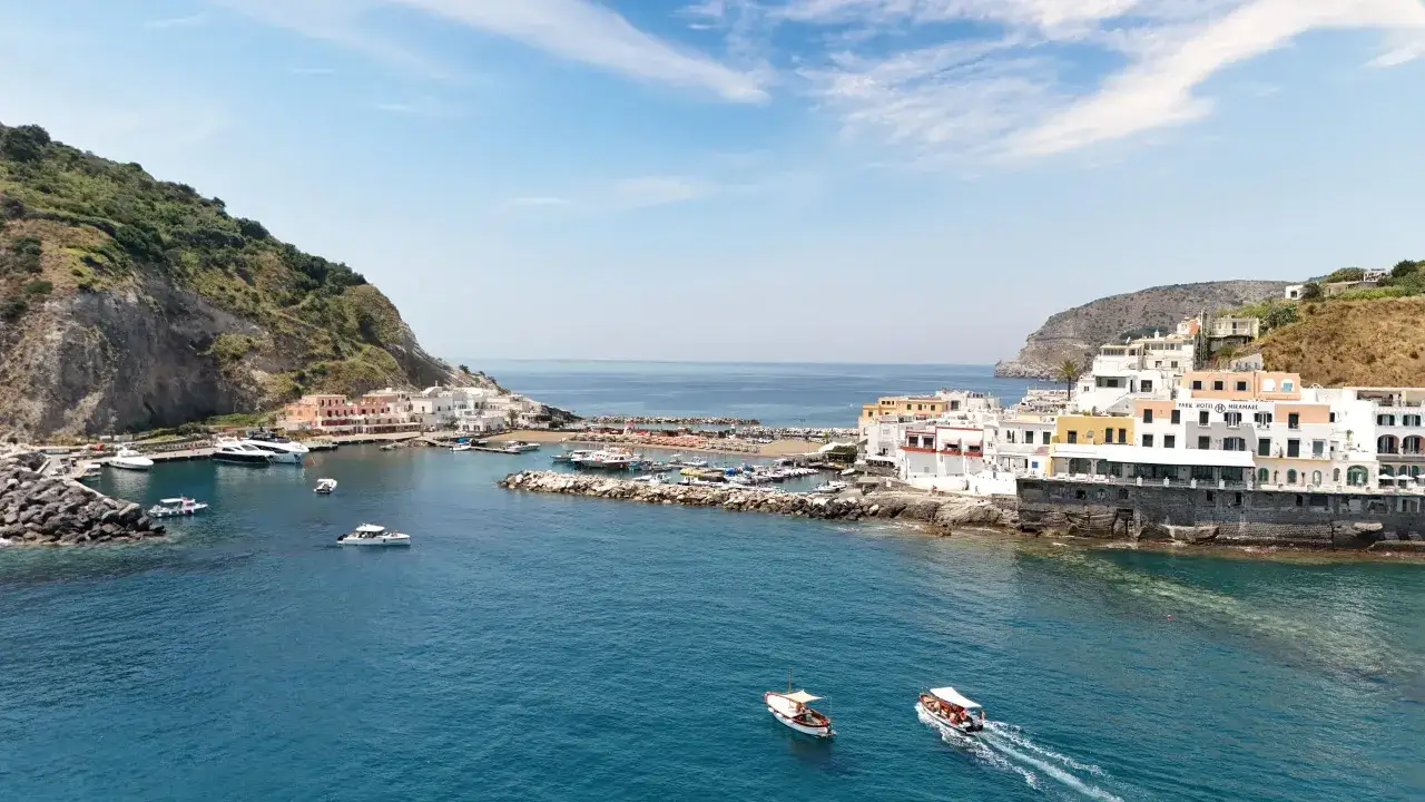 Vista aerea della spiaggia di Cava Ruffano con case bianche, barche e mare blu.
