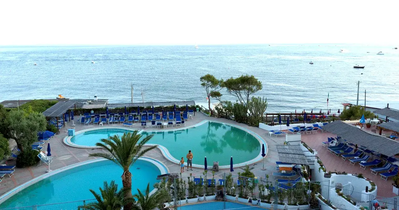 Piscine e lettini a Maronti Ischia, con il mare azzurro sullo sfondo e qualche barca all'orizzonte.