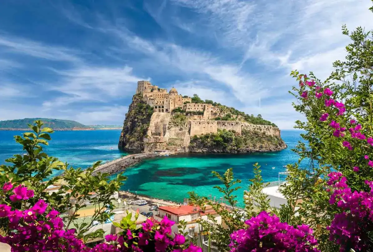 Castello Aragonese su scoglio a Ischia. Perfetto per chi cerca dove alloggiare a Ischia senza macchina, con mare cristallino e fiori viola.