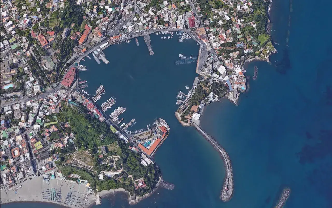 Vista aerea del porto turistico di Ischia, con numerose imbarcazioni ormeggiate e la città che si estende verso l'entroterra.