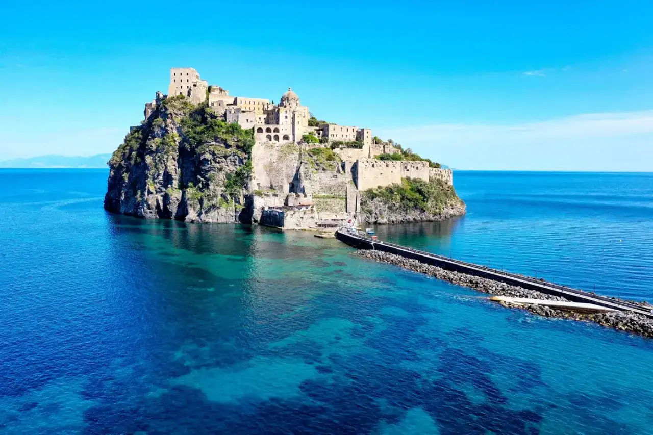 Castello Aragonese su isolotto roccioso, con pontile e mare cristallino. Scopri come arrivare alla spiaggia di Cartaromana per ammirare questo panorama.