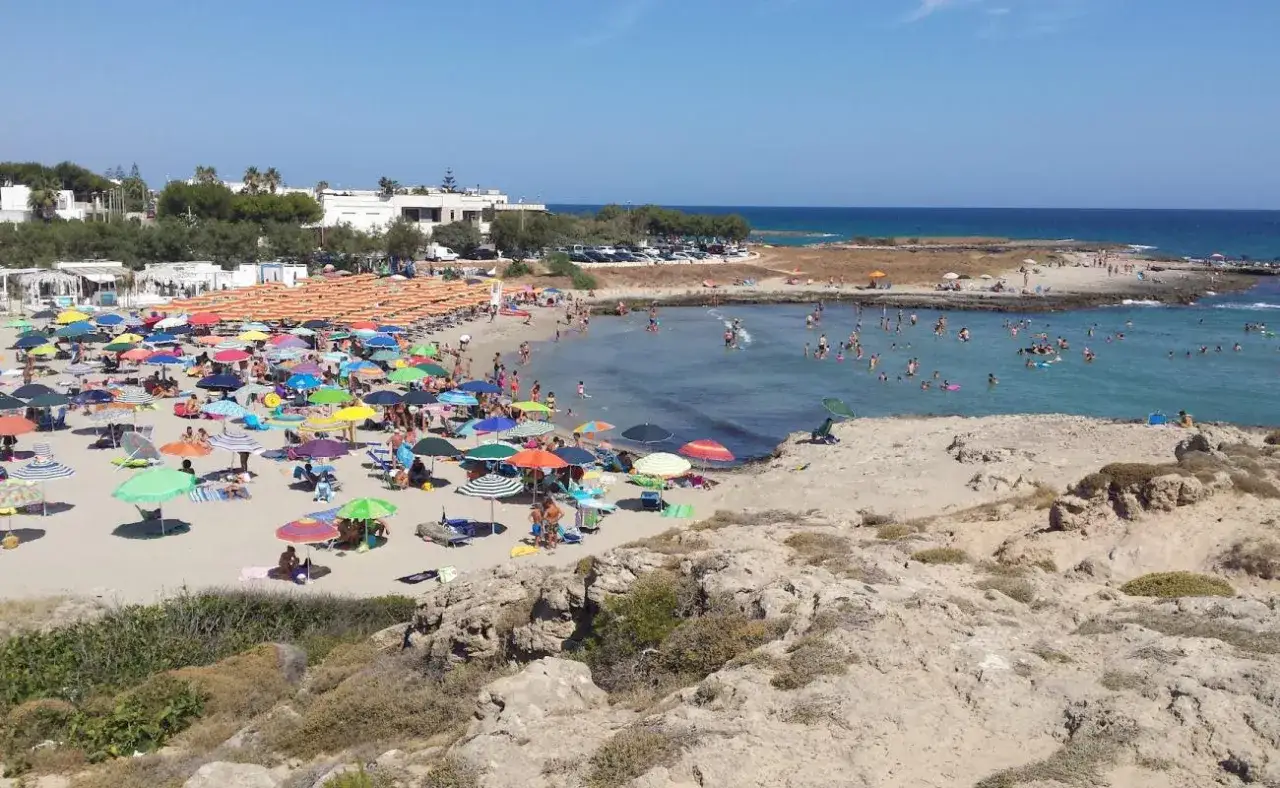 Una vivace riviera di San Montano gremita di ombrelloni colorati e bagnanti che si godono il mare cristallino sotto il sole estivo.