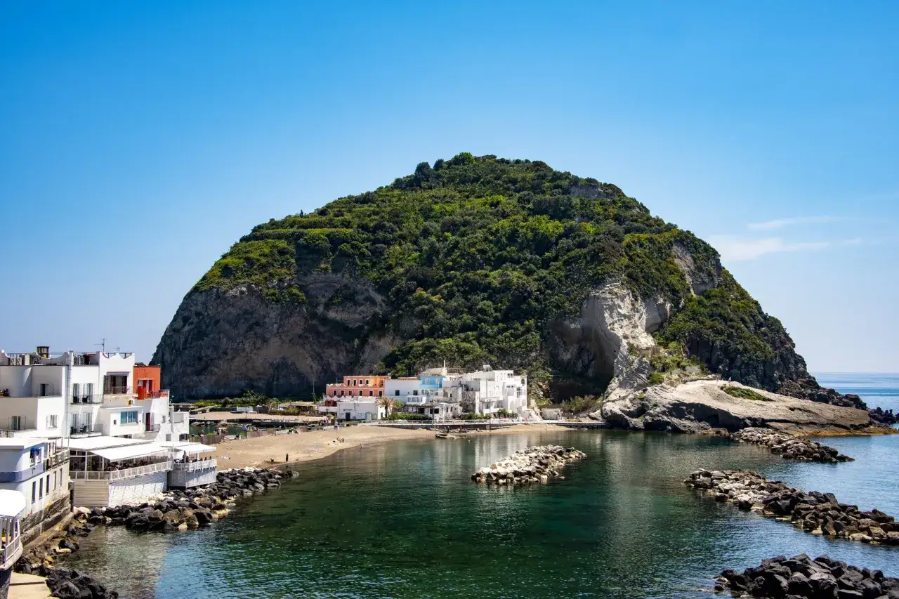La baia di Sant'Angelo, Ischia, con le sue case bianche affacciate sul mare cristallino e il promontorio verdeggiante.