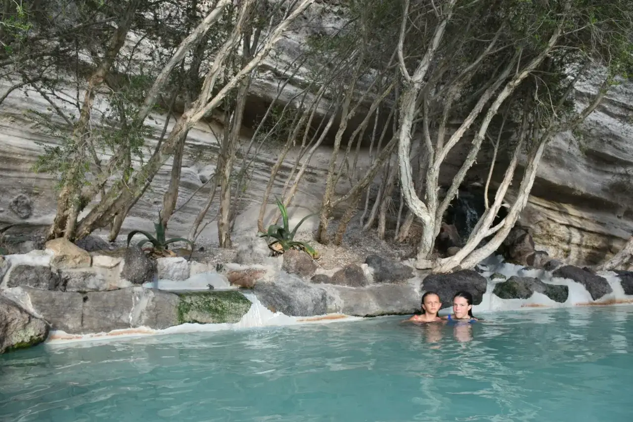 Due bambine si godono un bagno rilassante in una piscina naturale, circondata da rocce e vegetazione, un luogo perfetto per terme gratuite.