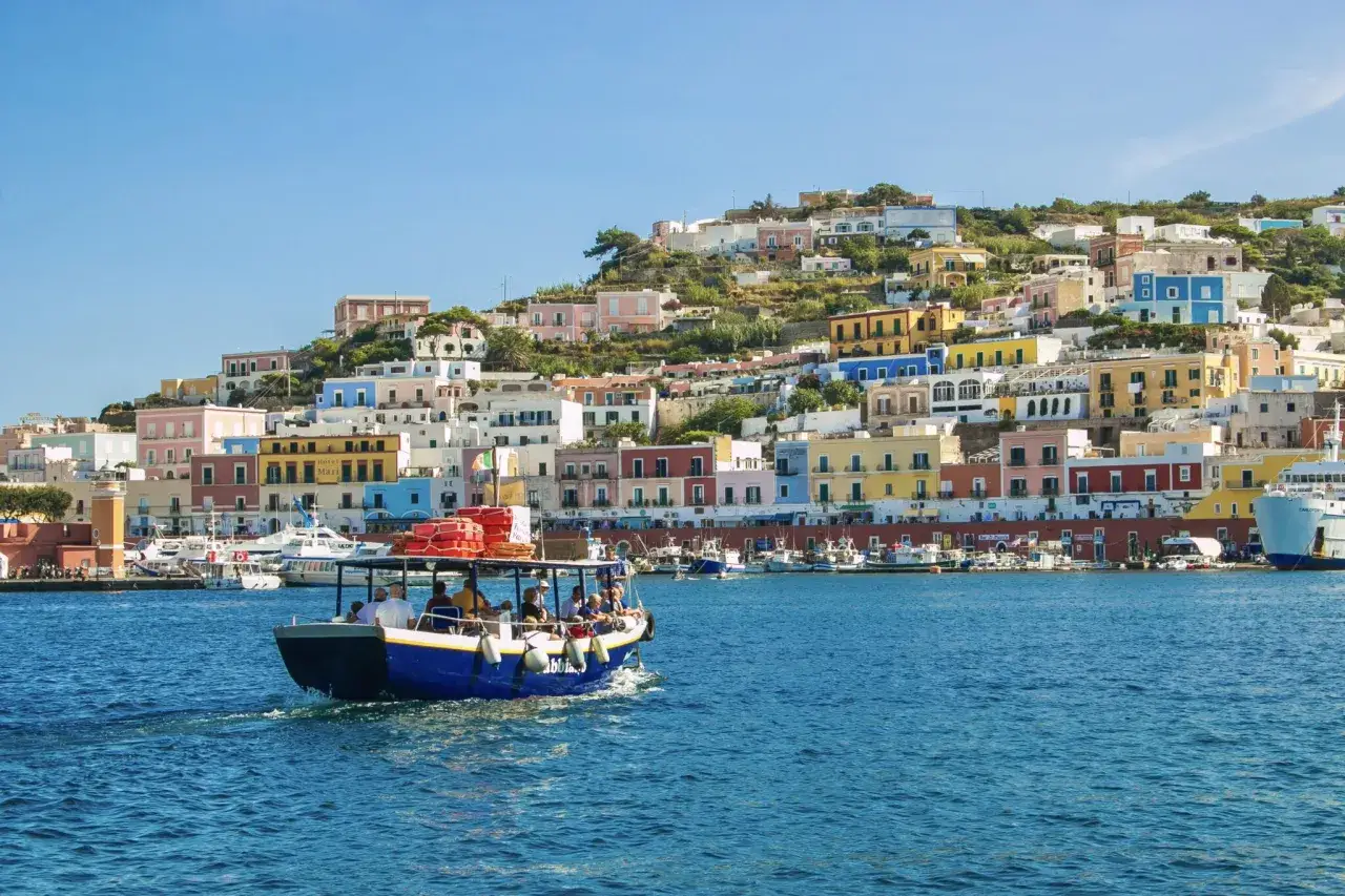 Barche e traghetti al molo Beverello di Napoli, con case colorate a picco sul mare.