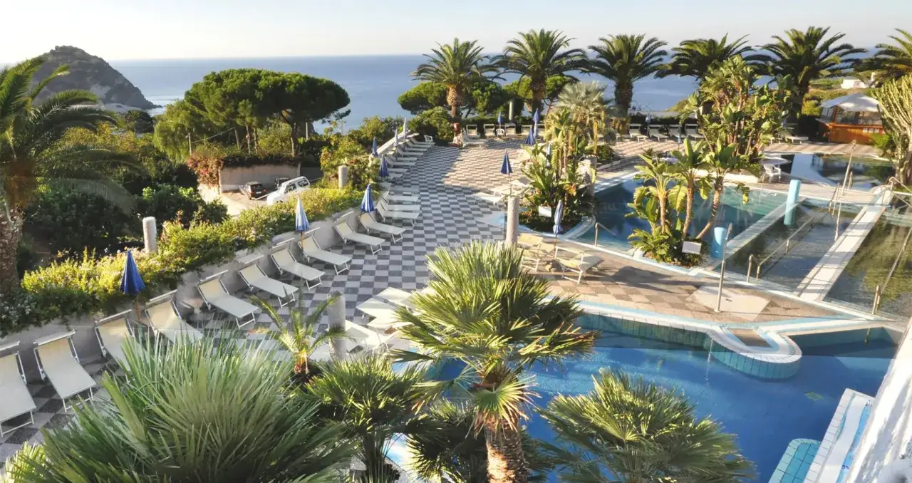 Un angolo tropicale di Ischia con piscine, palme e vista sul mare. Un paradiso per rilassarsi.