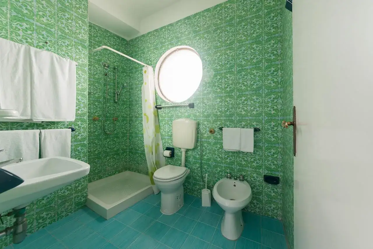 Bagno colorato con piastrelle verdi e pavimento turchese. Doccia, WC, bidet e lavandino. Un assaggio del hotel Antonella Ischia.