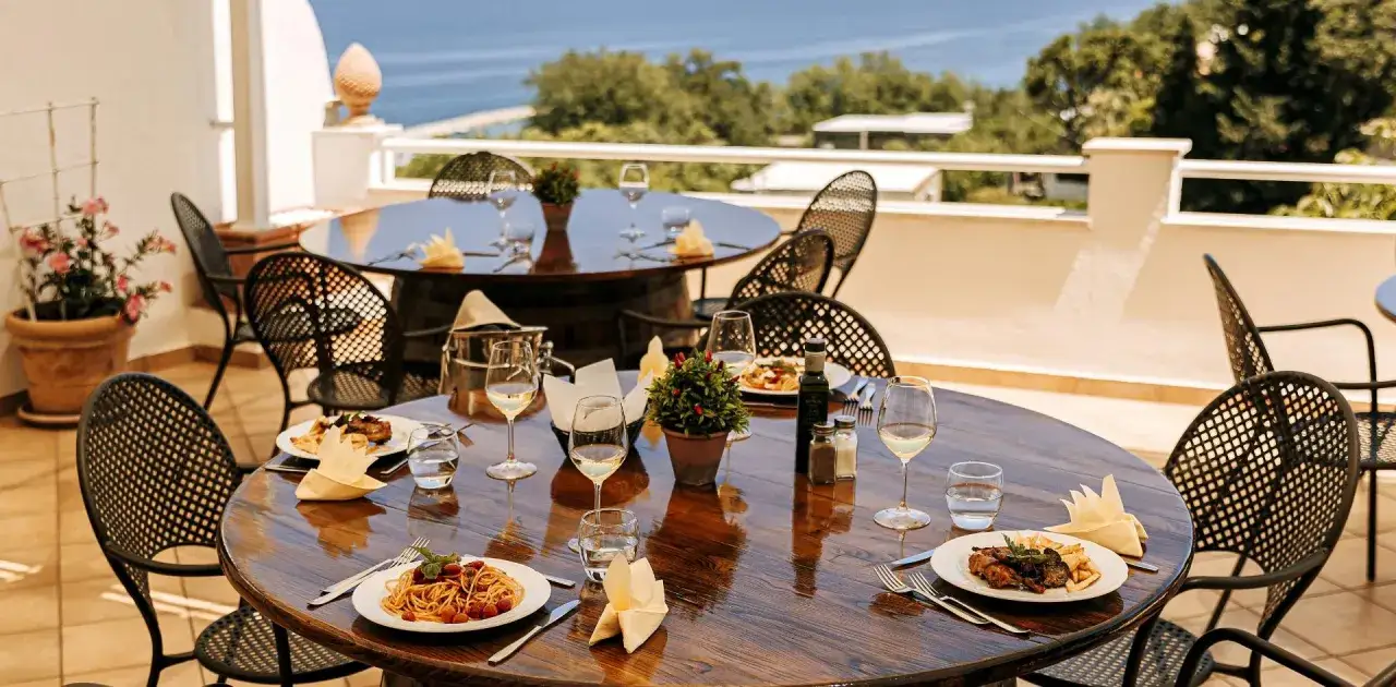 Tavoli apparecchiati con piatti di pasta e carne, bicchieri di vino e vista mare. Un'atmosfera perfetta per i ristoranti di Casamicciola.