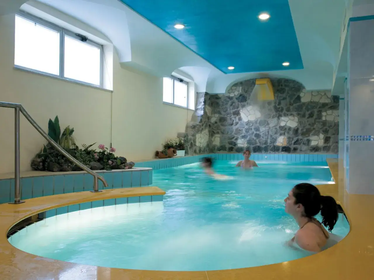Relax in una piscina termale ad Alexander Ischia, con cascata e piante rigogliose.