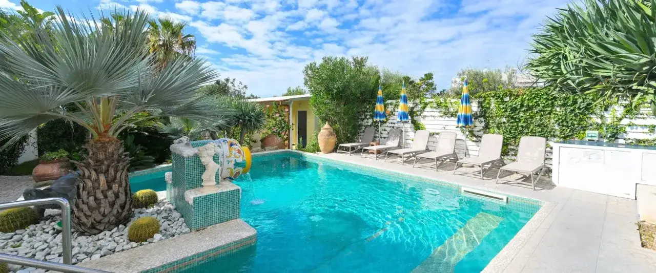 Piscina cristallina e lettini prendisole al hotel La Villa Ischia, circondati da palme e vegetazione lussureggiante.