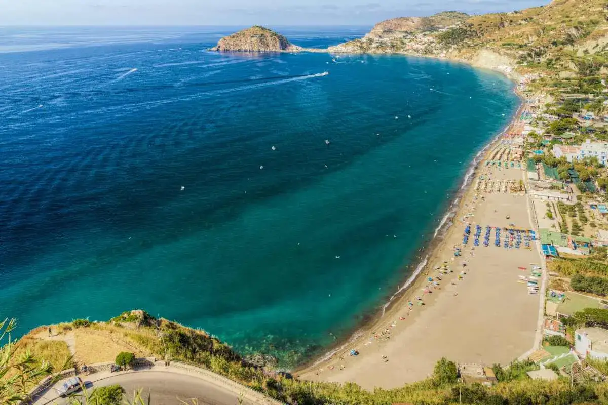 Vista aerea della spiaggia dei Maronti con lidi attrezzati, ombrelloni colorati e il mare turchese.