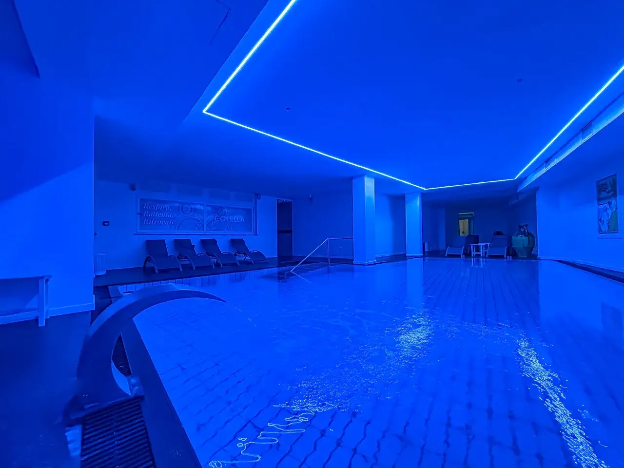 Piscina interna illuminata di blu, con lettini e la scritta 