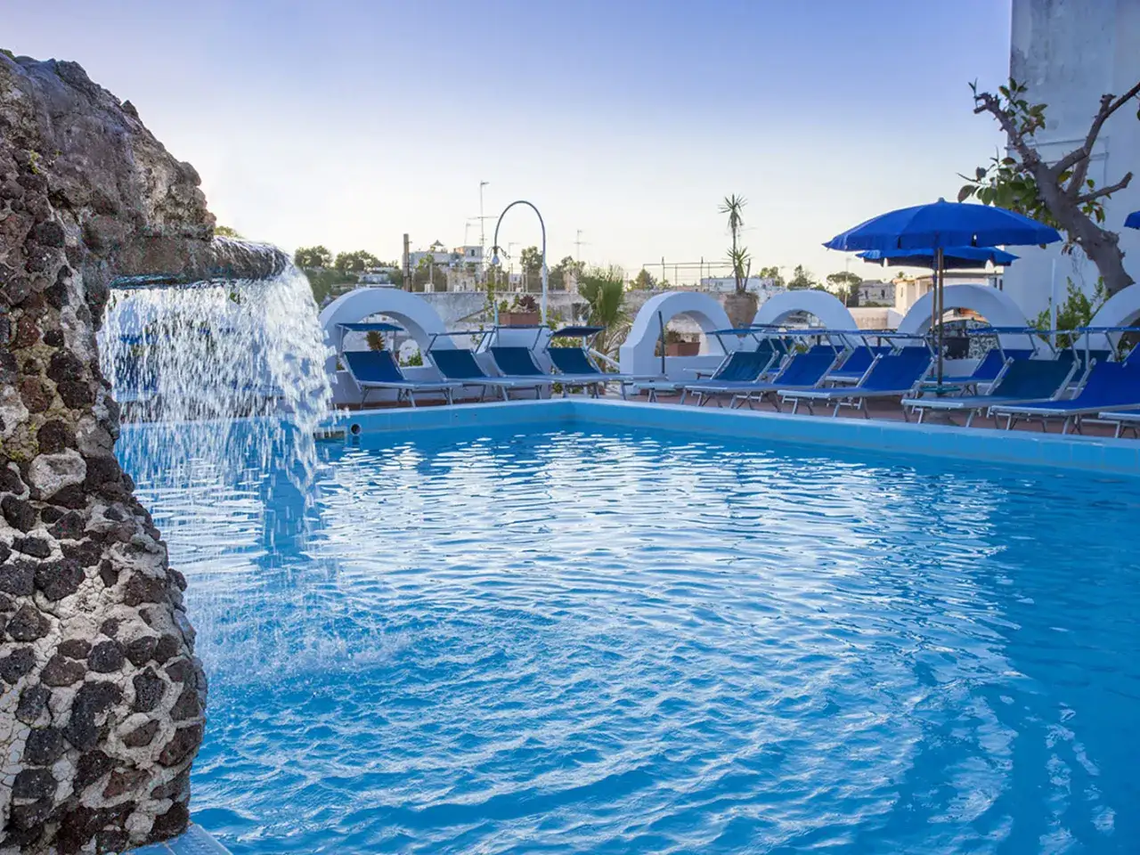 Piscina con cascata e lettini prendisole al hotel terme Tirrenia Ischia. Relax e sole ti aspettano.