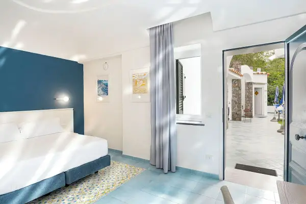 Camera luminosa con letto matrimoniale e vista su un cortile con ombrelloni blu. Un invito a soggiornare all'hotel oasi Ischia.